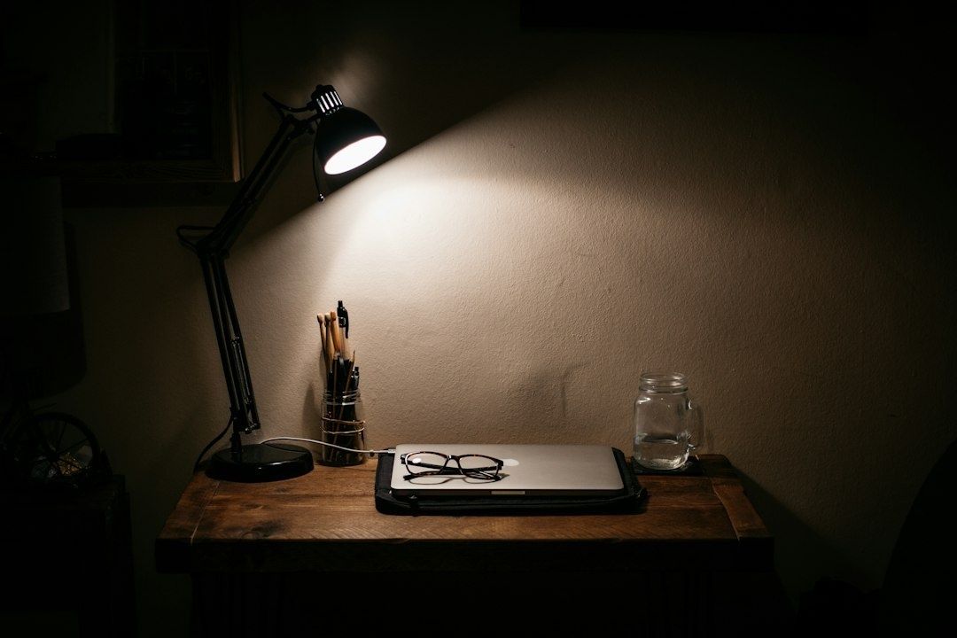 Skrivbord med riktad arbetslampa, laptop, glasögon och pennor